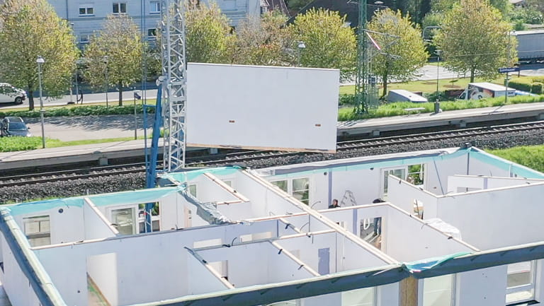 Large wall panel hoisted by a crane over a building under construction